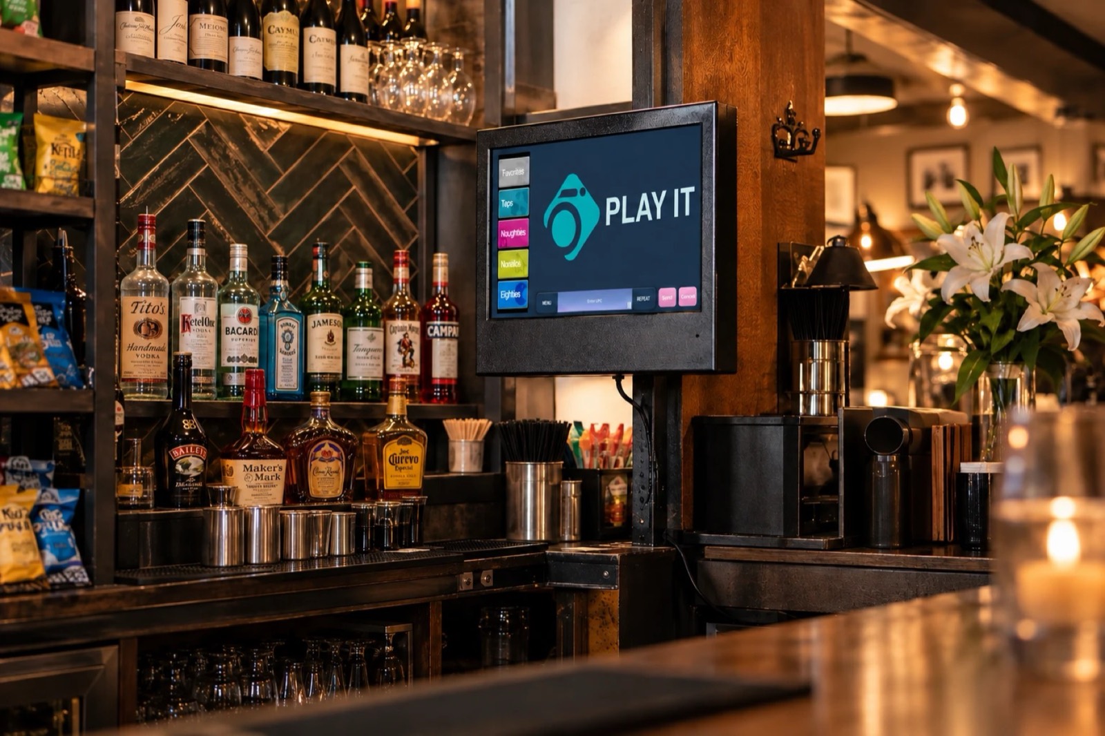 Wall-mounted iO touchscreen behind a bar showing the Play It music selection screen