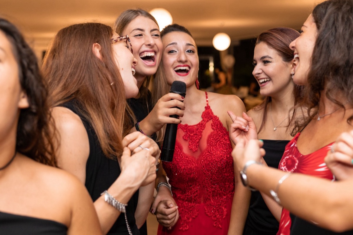 Group of friends laughing and singing together around one microphone