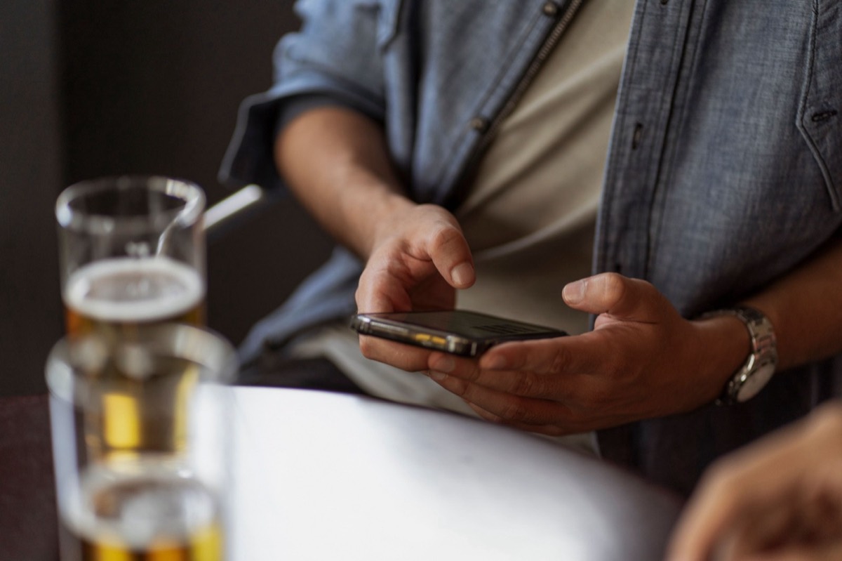 Customer using their phone at a pub table with a pint