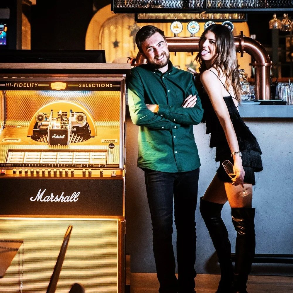 Couple posing beside a Marshall jukebox at the bar