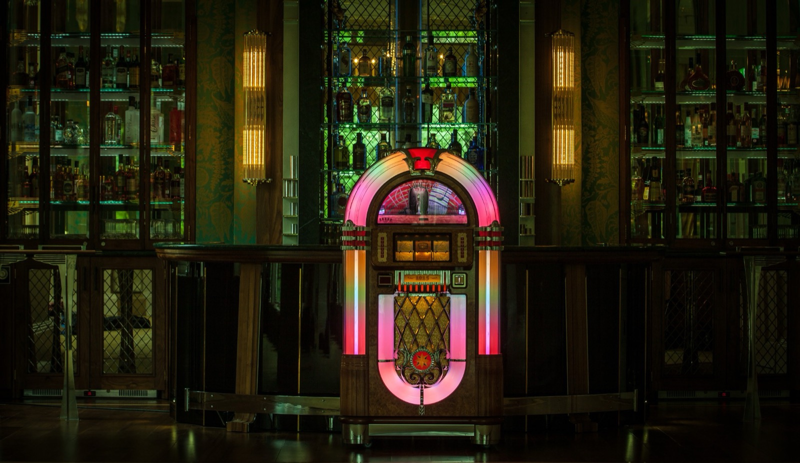 Classic jukebox glowing pink and amber in front of a dark, elegant cocktail bar