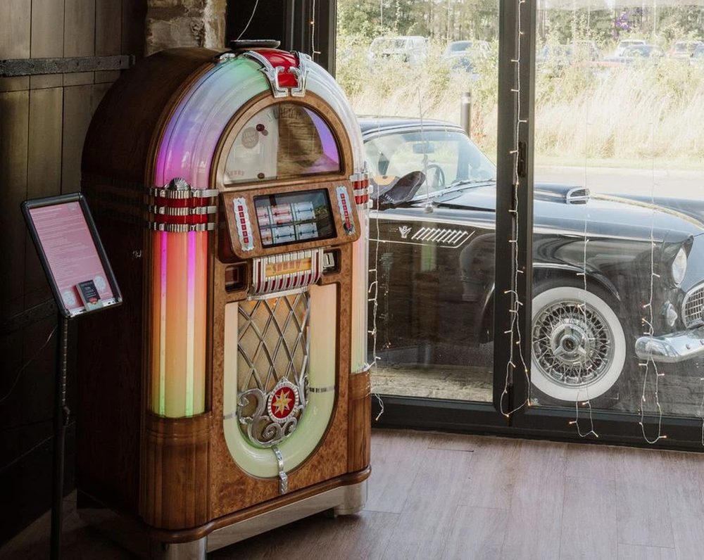Classic jukebox glowing beside a window with a vintage car outside