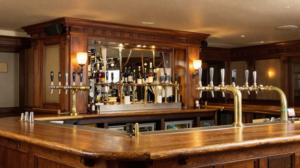 A traditional pub bar with brass hand pulls and a warm, wood panelled back bar