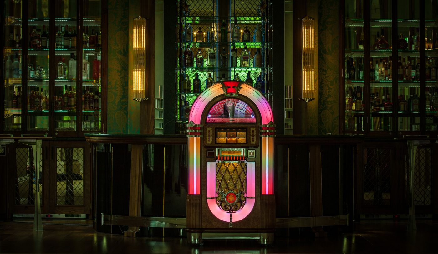 Illuminated classic jukebox glowing pink in front of a dark art deco cocktail bar