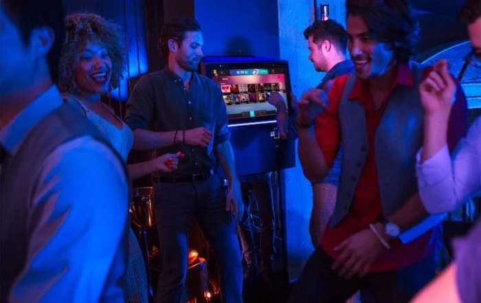 Customers dancing in a lively bar beside a digital jukebox