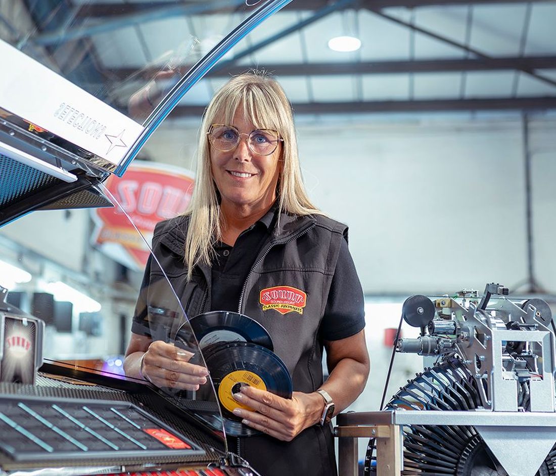Sound Leisure team member holding vinyl records beside a jukebox in the workshop